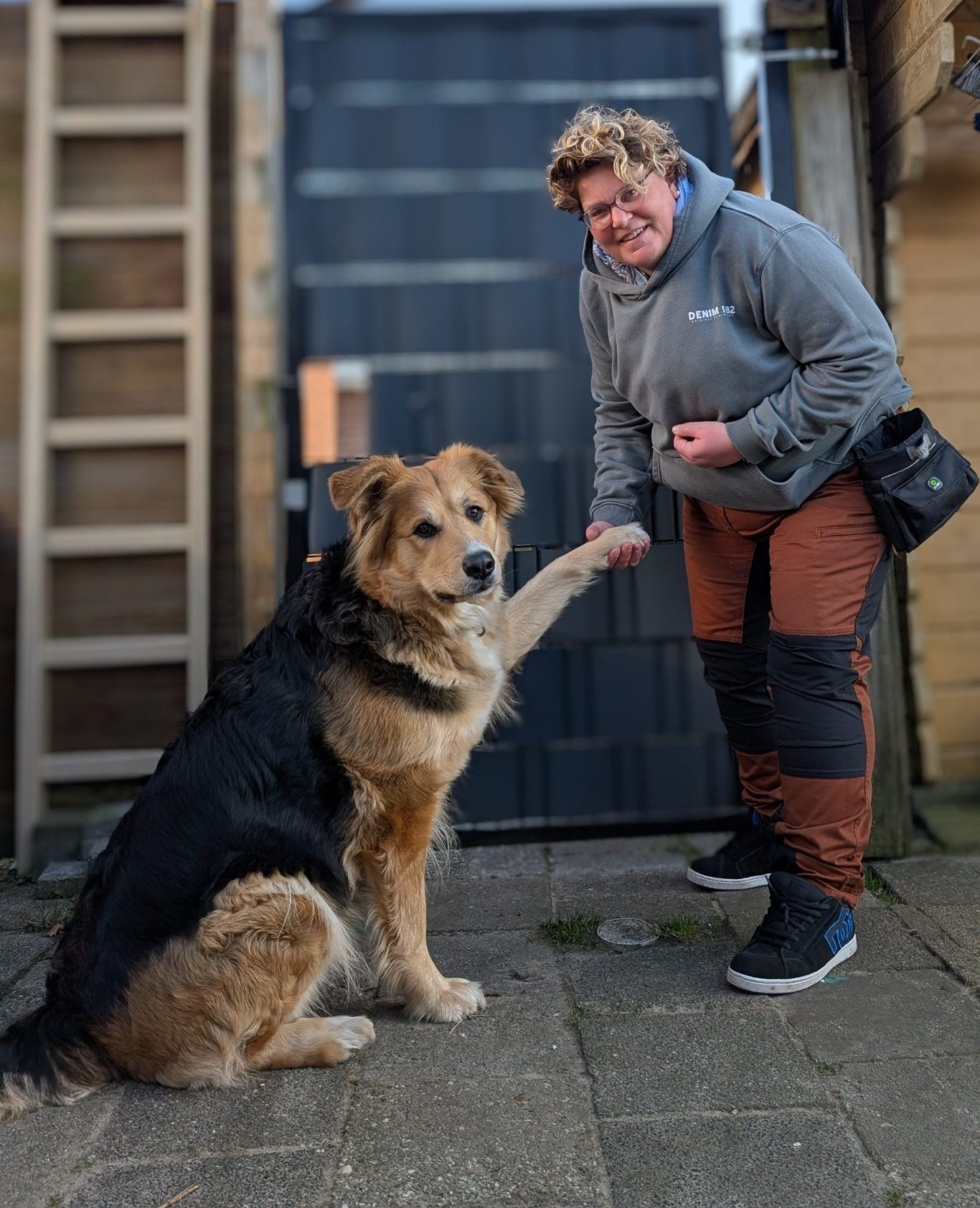 trainer met hond Man in een zwart shirt staat naast een blije zwarte hond in een groen veld.
